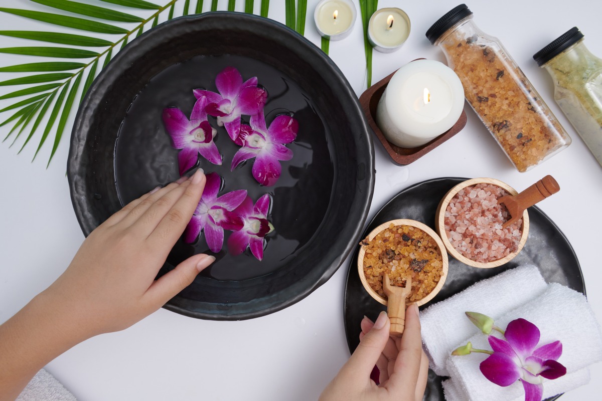 young-woman-applying-natural-scrub-hands-against-white-surface-spa-treatment-product-female-hand-spa-massage-perfumed-flowers-water-candles-relaxation-flat-lay-top-view